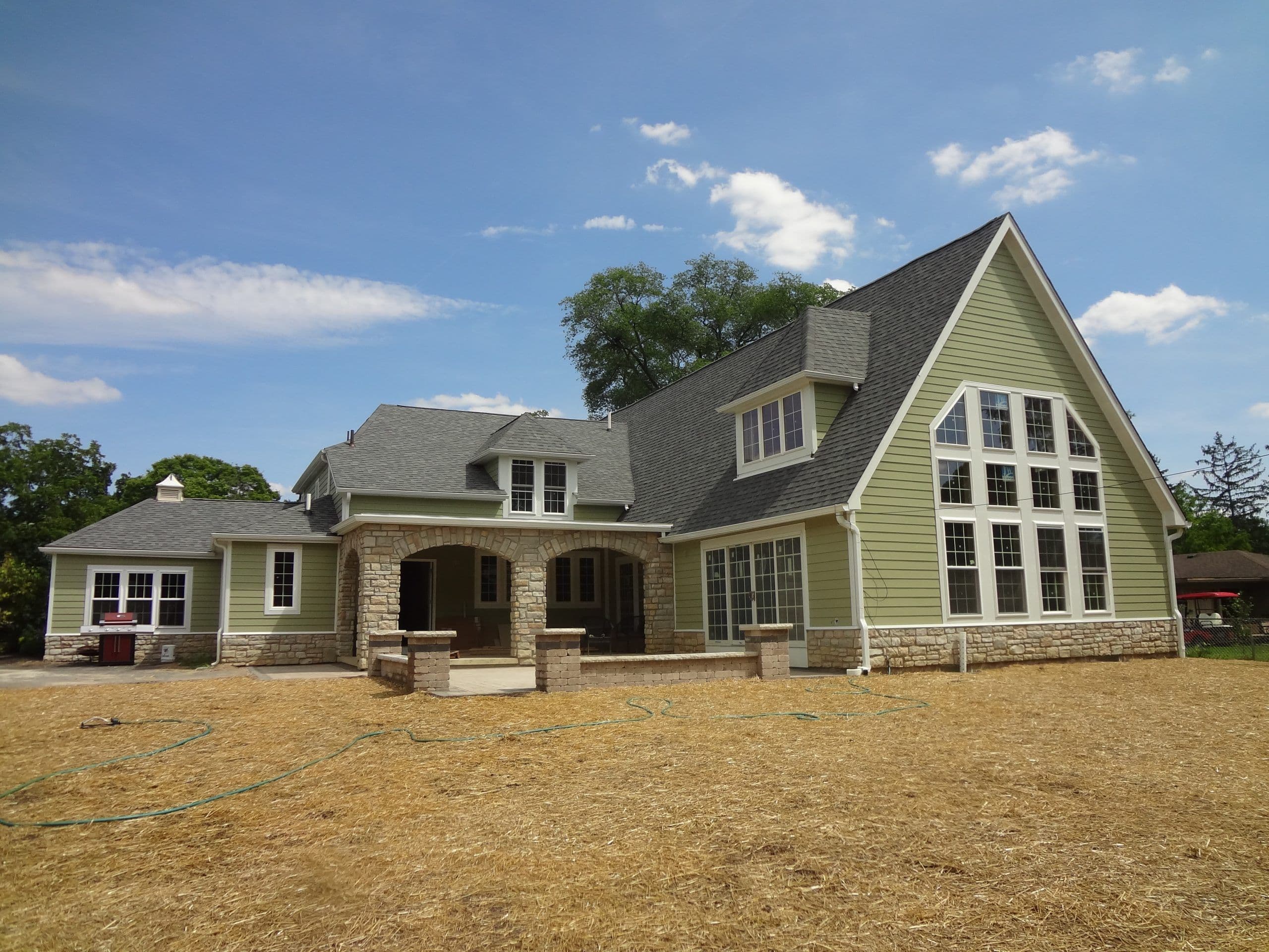 Newly built custom home in Central Ohio with sage lap siding, a stone arched porch, dormers and a two-story gable of divided-light windows.